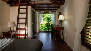 Una habitación con techo de madera, una cama, un escritorio con lámpara, una silla y vistas a zonas verdes.