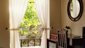 Una habitación con techo de madera, ventana con cortinas de gasa, una mesita con un espejo y un cuadro enmarcado en la pared.