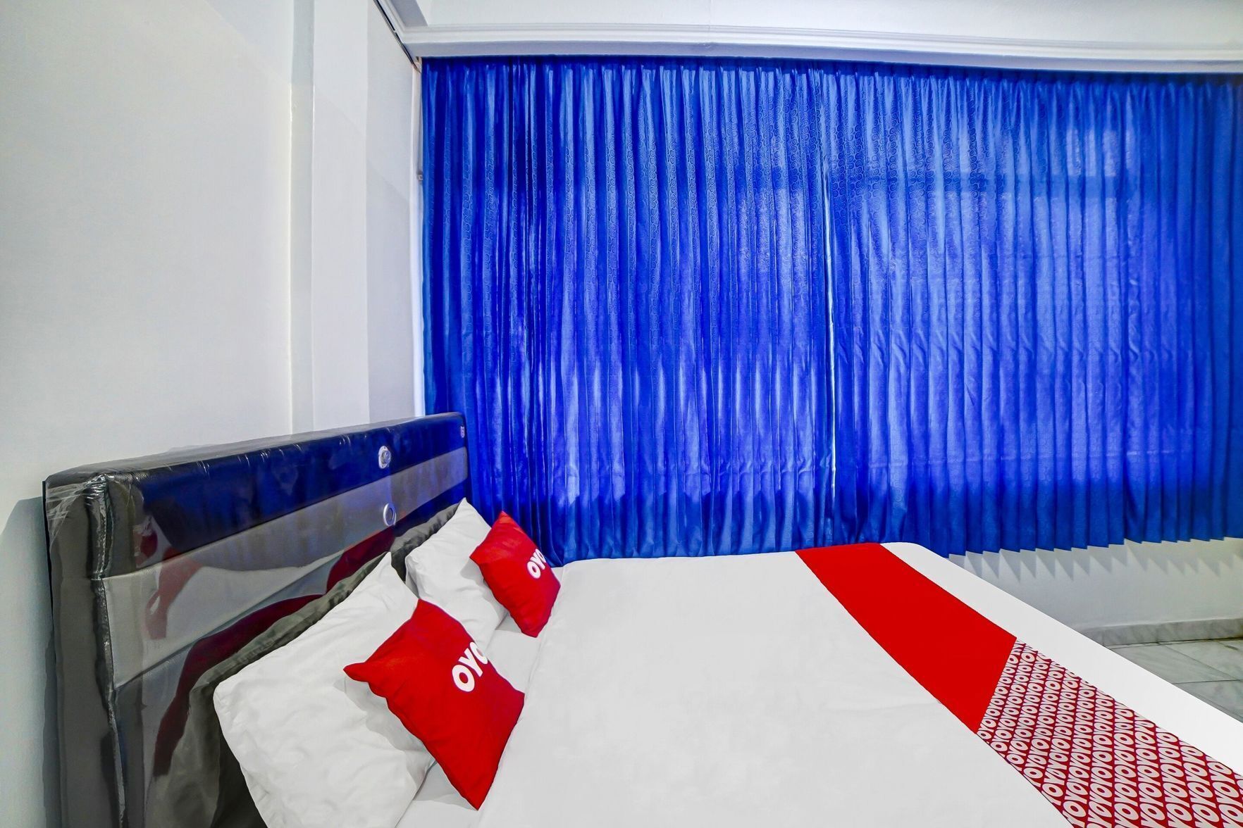 A hotel room with a bed, blue curtains, and a white and red bedspread.