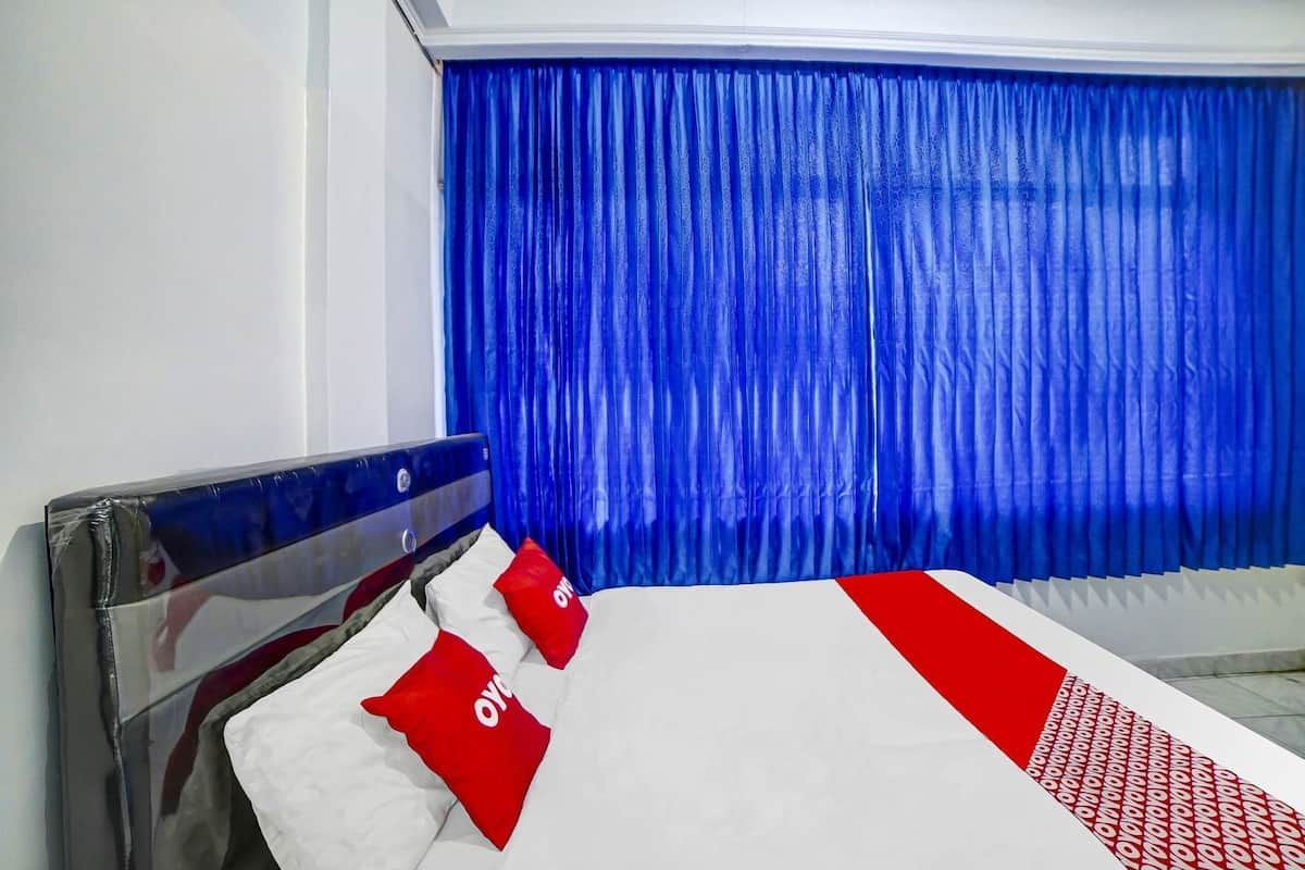 A hotel room with a bed, blue curtains, and a white and red bedspread.