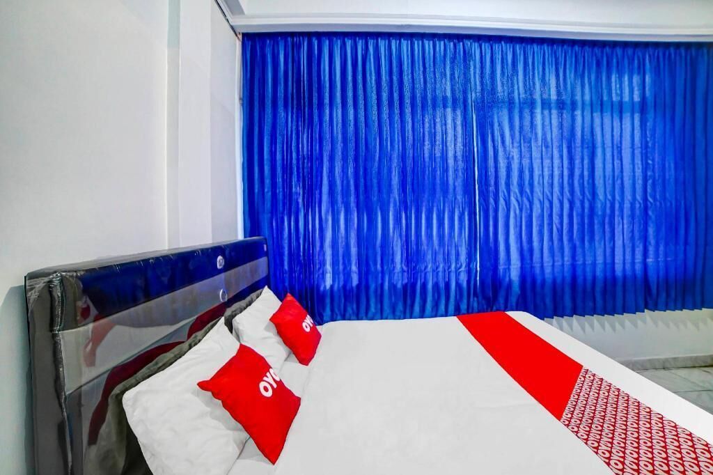 A hotel room with a bed, blue curtains, and red and white bedding.