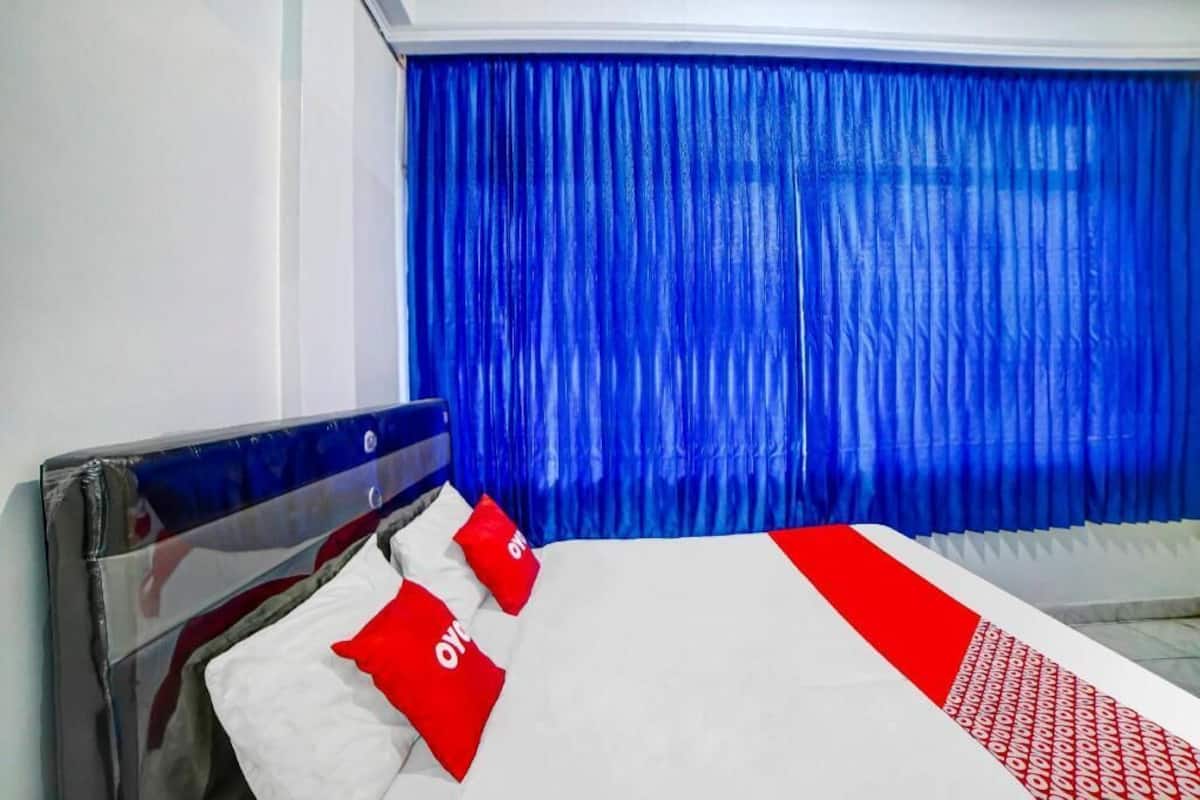 A hotel room with a bed, blue curtains, and red and white bedding.