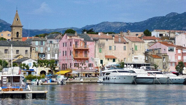 A coastal town with colorful buildings, a church tower, and boats docked at the harbor.