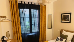 A hotel room with a bed, a bedside table with a lamp, a mirror, and a window with curtains.