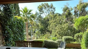 A patio with a round table and chairs, surrounded by lush greenery and trees.