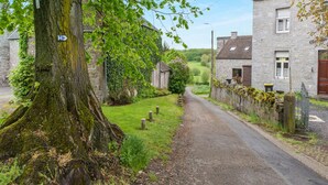 A narrow rural road flanked by stone houses with ivy-covered walls and a large tree with moss. - Charming holiday home in Clavier with garden (Clavier)