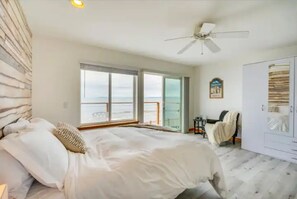 Un dormitorio con cama, ventilador de techo, armario y vistas al mar a través de amplios ventanales.