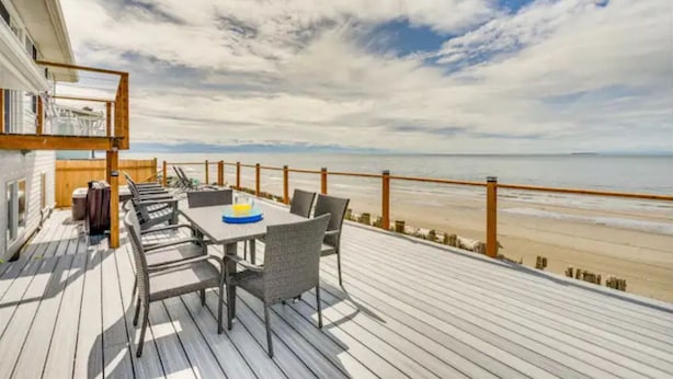 A deck with a table and chairs overlooking a beach.