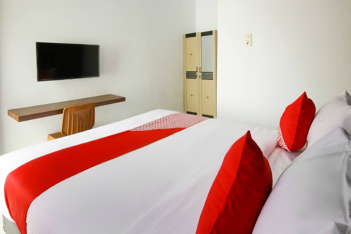 A hotel room with a bed, a TV mounted on the wall, a wardrobe, and a desk with a chair.