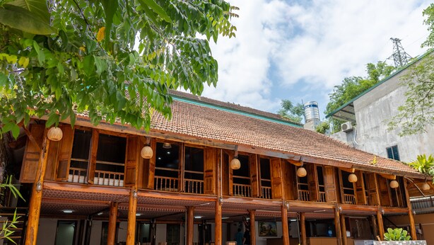 A traditional wooden building with a tiled roof, multiple balconies, and outdoor seating areas. - Odyssey Hostel, Tours & Motorbikes Rental (Ha Giang 1)