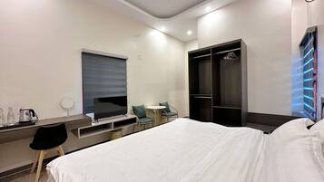 A modern hotel room with a large bed, a desk with a flat-screen TV, a seating area with chairs, and a wardrobe with a mirror.