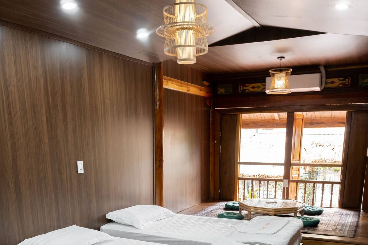 A hotel room with three beds, wooden flooring, and a large window with a view.