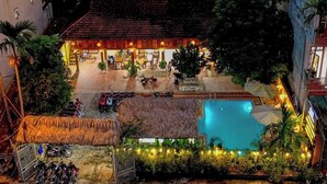 A two-story building with a swimming pool, outdoor seating, and a thatched-roof structure. - Odyssey Hostel, Tours & Motorbikes Rental (Ha Giang 1)