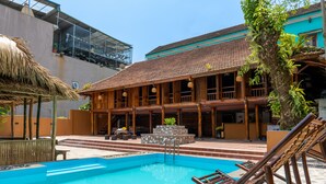 A pool area with a wooden deck, lounge chairs, and a thatched roof structure. - Odyssey Hostel, Tours & Motorbikes Rental (Ha Giang 1)