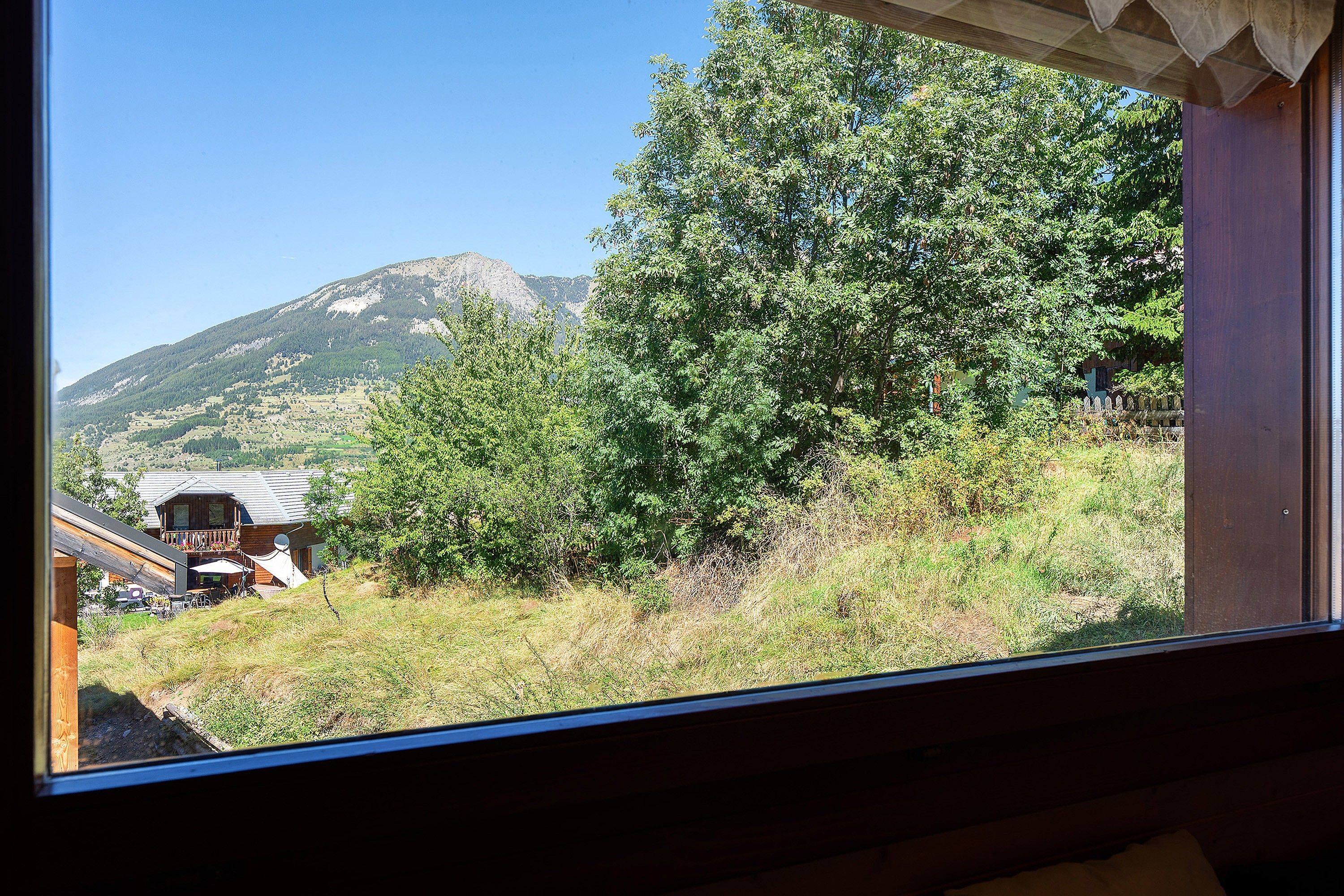 Une vue à travers une fenêtre sur un paysage de montagne, avec une maison et une terrasse en bois.