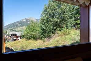 Une vue à travers une fenêtre sur un paysage de montagne, avec une maison et une terrasse en bois.