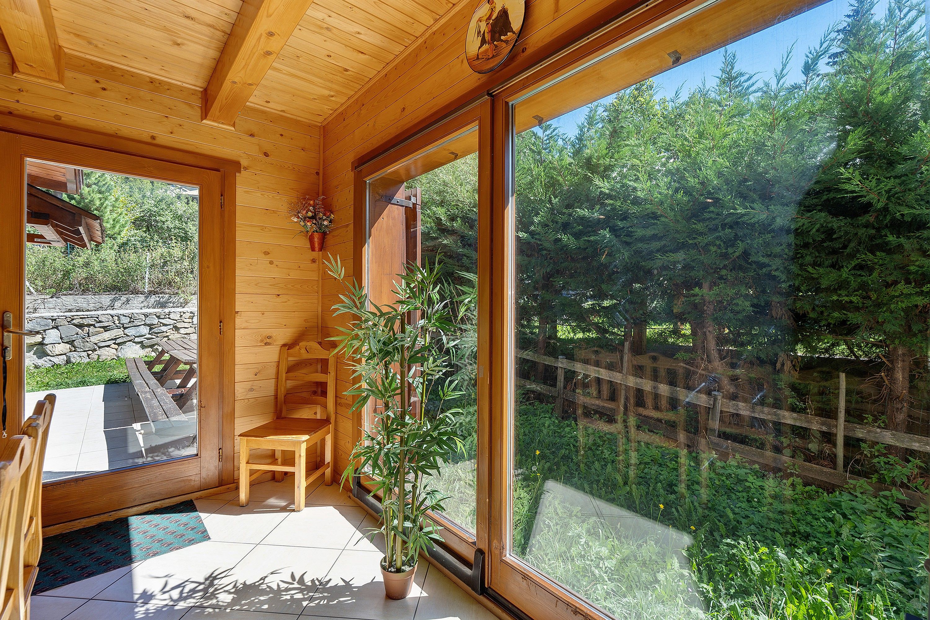 Un interior de madera con un gran ventanal, una silla y una planta en maceta.
