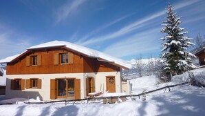 A wooden chalet with a snow-covered roof, a large window, and a door.
