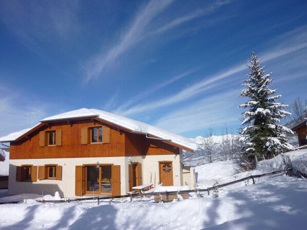 Un chalet en bois avec un toit enneigé, une grande fenêtre et une porte.