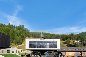 Een modern gebouw met een glazen gevel, aangeduid met 'PIC VERT', gelegen in een bergachtig gebied, met een skilift zichtbaar op de achtergrond.