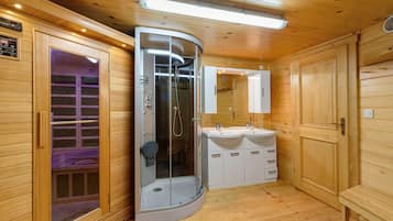 Een moderne, compacte badkamer met een douchecabine van glas, een wastafel met twee wasbakken en houten lambrisering.
