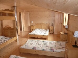 Une chambre dans un chalet en bois, avec des lits superposés, un lit simple, des tables de chevet, des lampes et une fenêtre.