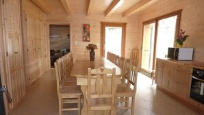 A wooden interior with a long dining table and chairs, a kitchen area with cabinets, and a window providing natural light.