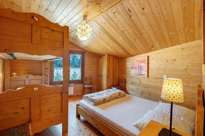 A wooden cabin bedroom with a bed, a chair, a lamp, and a painting on the wall.