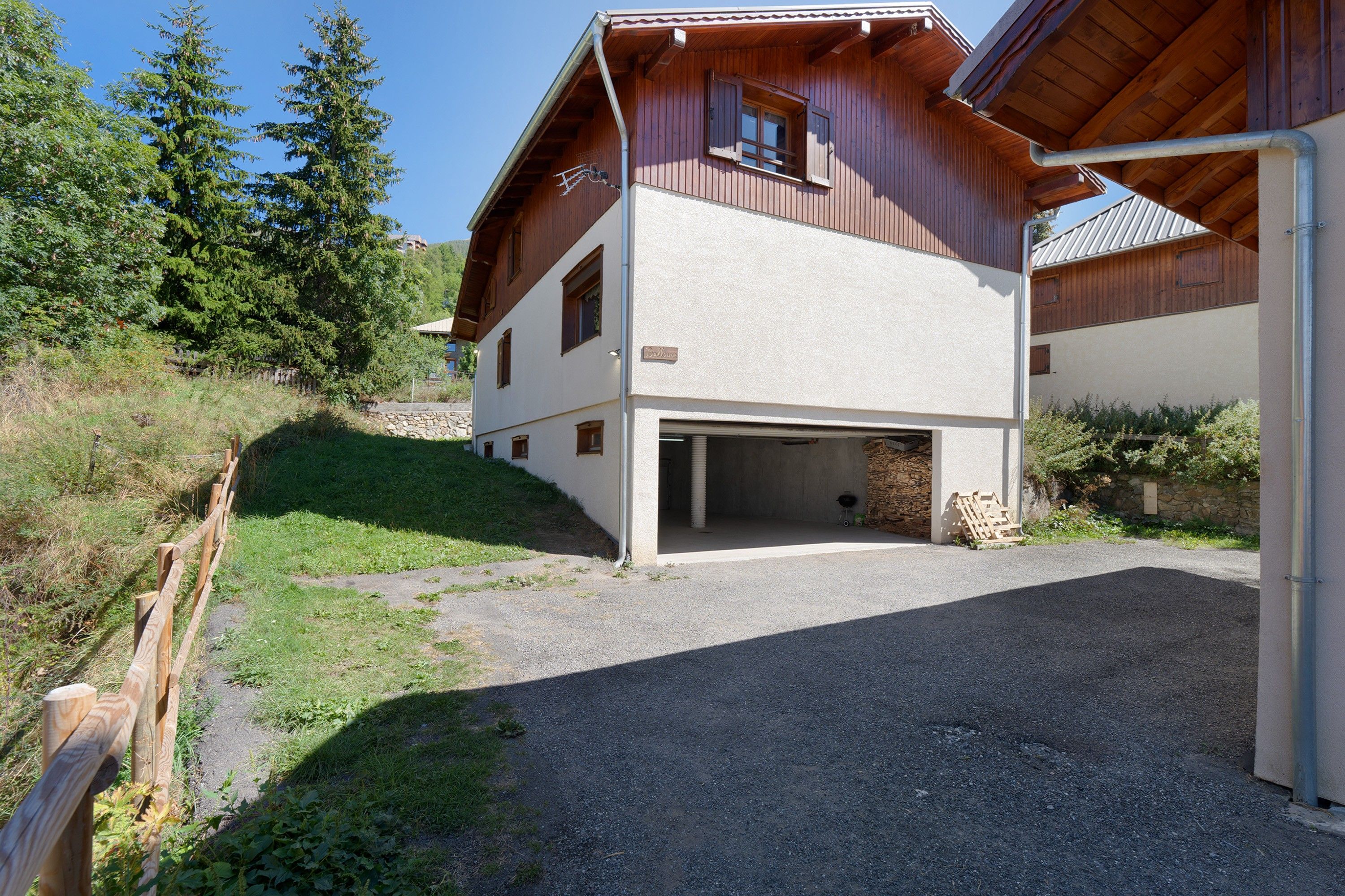 Ein zweistöckiges Gebäude mit Garage, umgeben von Grünflächen und einer Steinmauer.