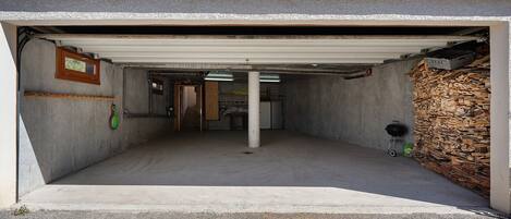 Eine Garage mit Betonboden, einer Holztür und einem Holzstapel auf der rechten Seite.