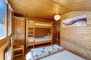 Een houten kamer met stapelbedden, een kledingkast, een klein tafeltje en een schilderij aan de muur.