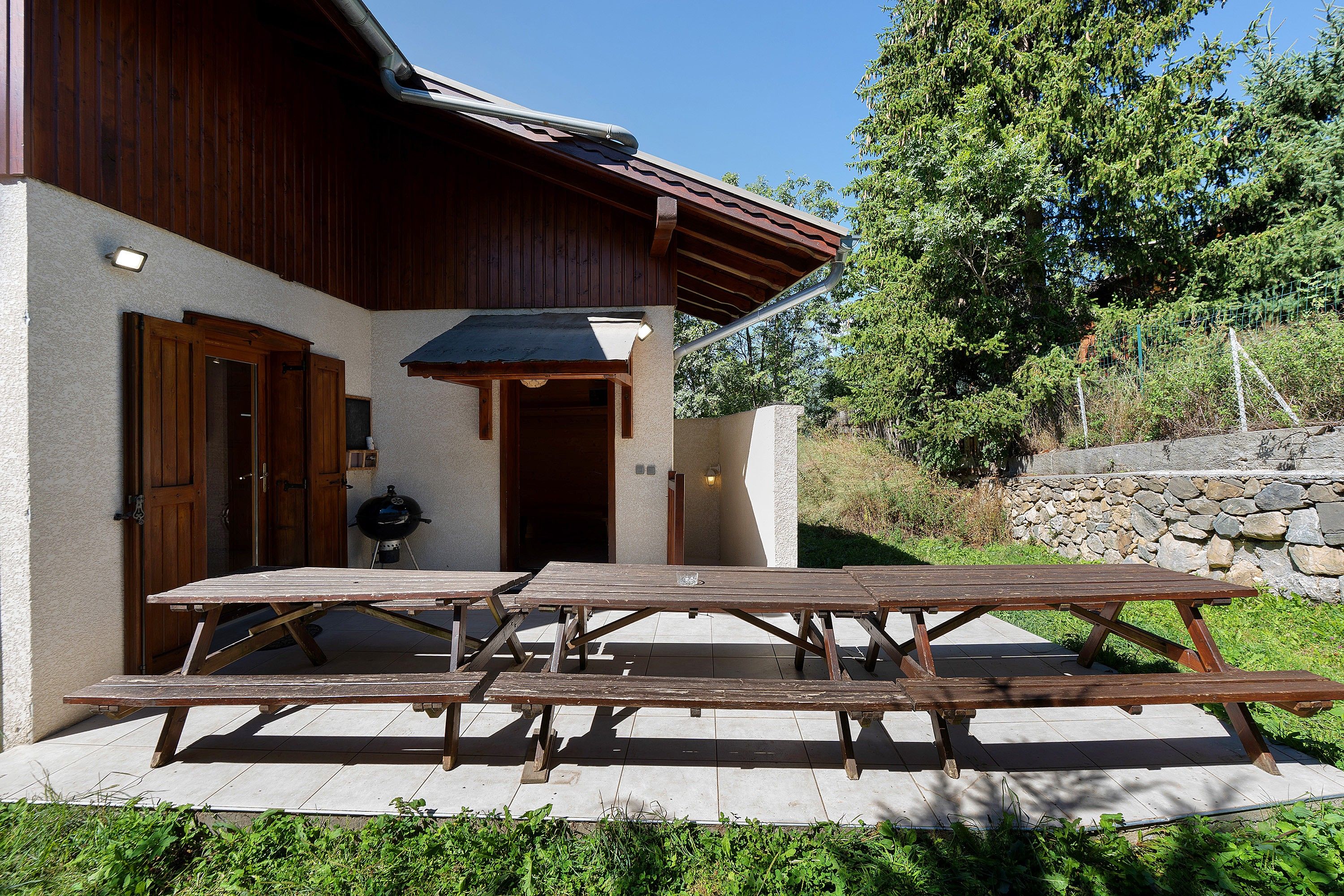 A wooden building with a covered patio area, a barbecue grill, and a stone wall.