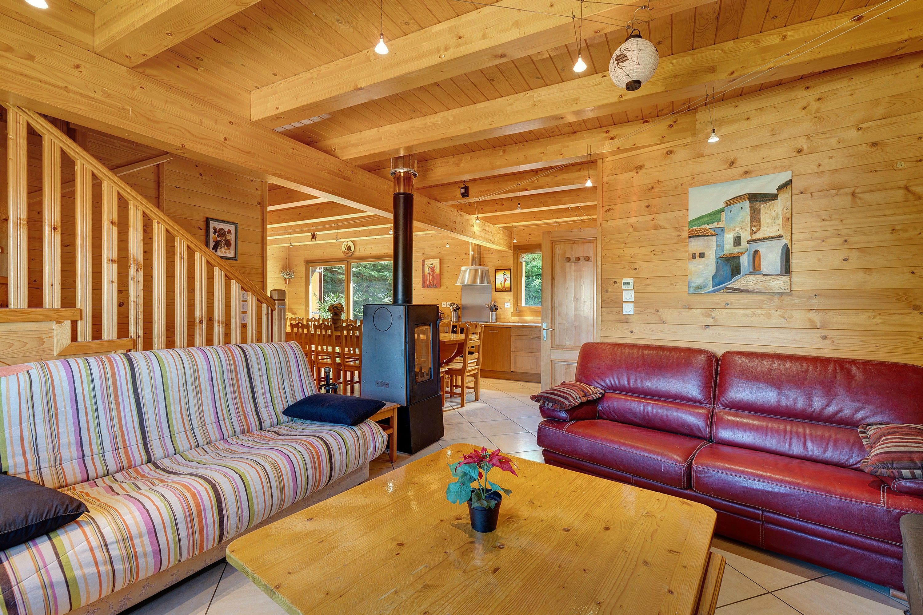 Un intérieur en bois avec un canapé à rayures, un canapé en cuir rouge et une table basse en bois agrémentée d’une plante.