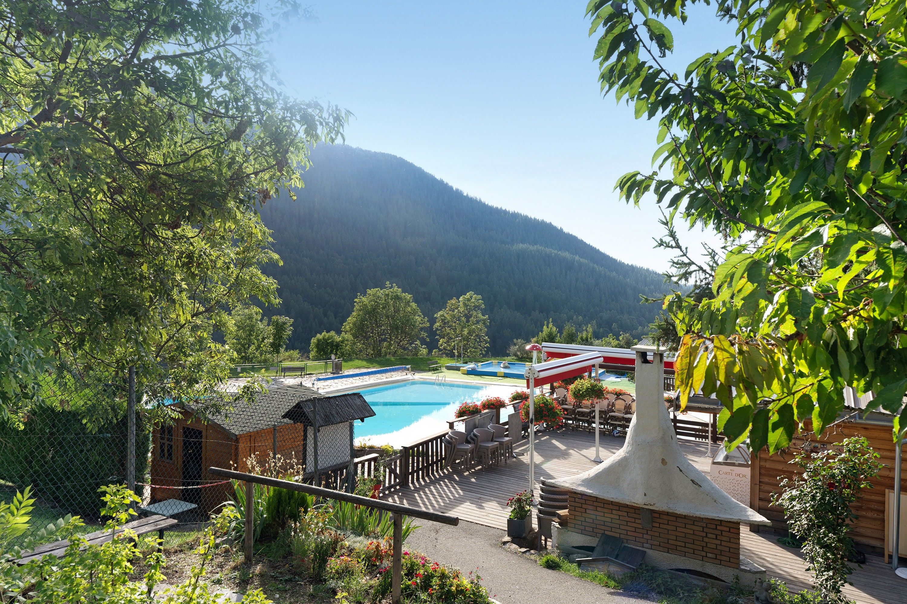 A pool area with a wooden deck, lounge chairs, and a mountain backdrop.