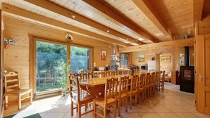 Un intérieur spacieux en bois, avec une grande table à manger entourée de chaises, un coin cuisine et une porte-fenêtre coulissante donnant sur un jardin.