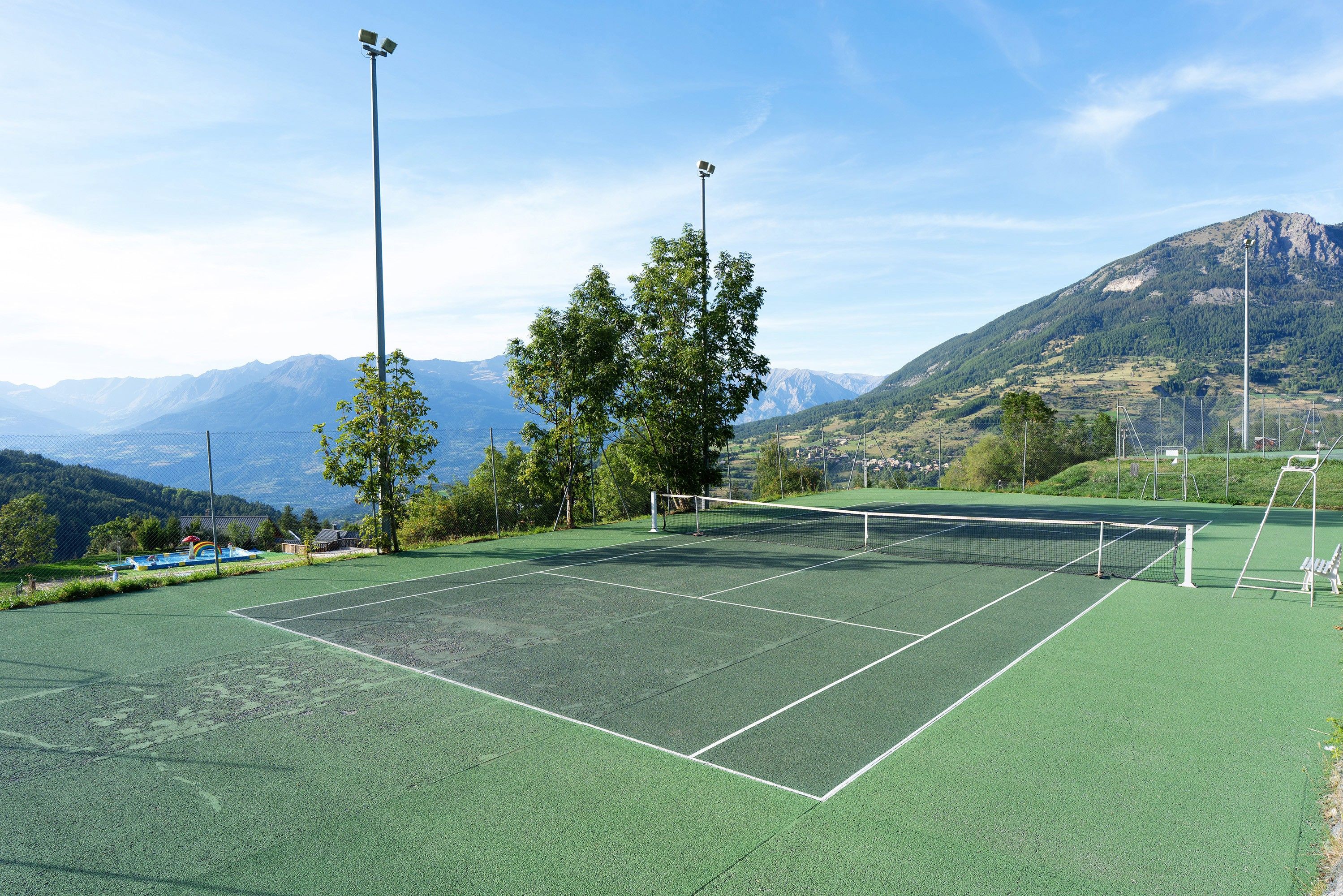 Un court de tennis avec un filet, entouré d’arbres et avec des montagnes en arrière-plan.