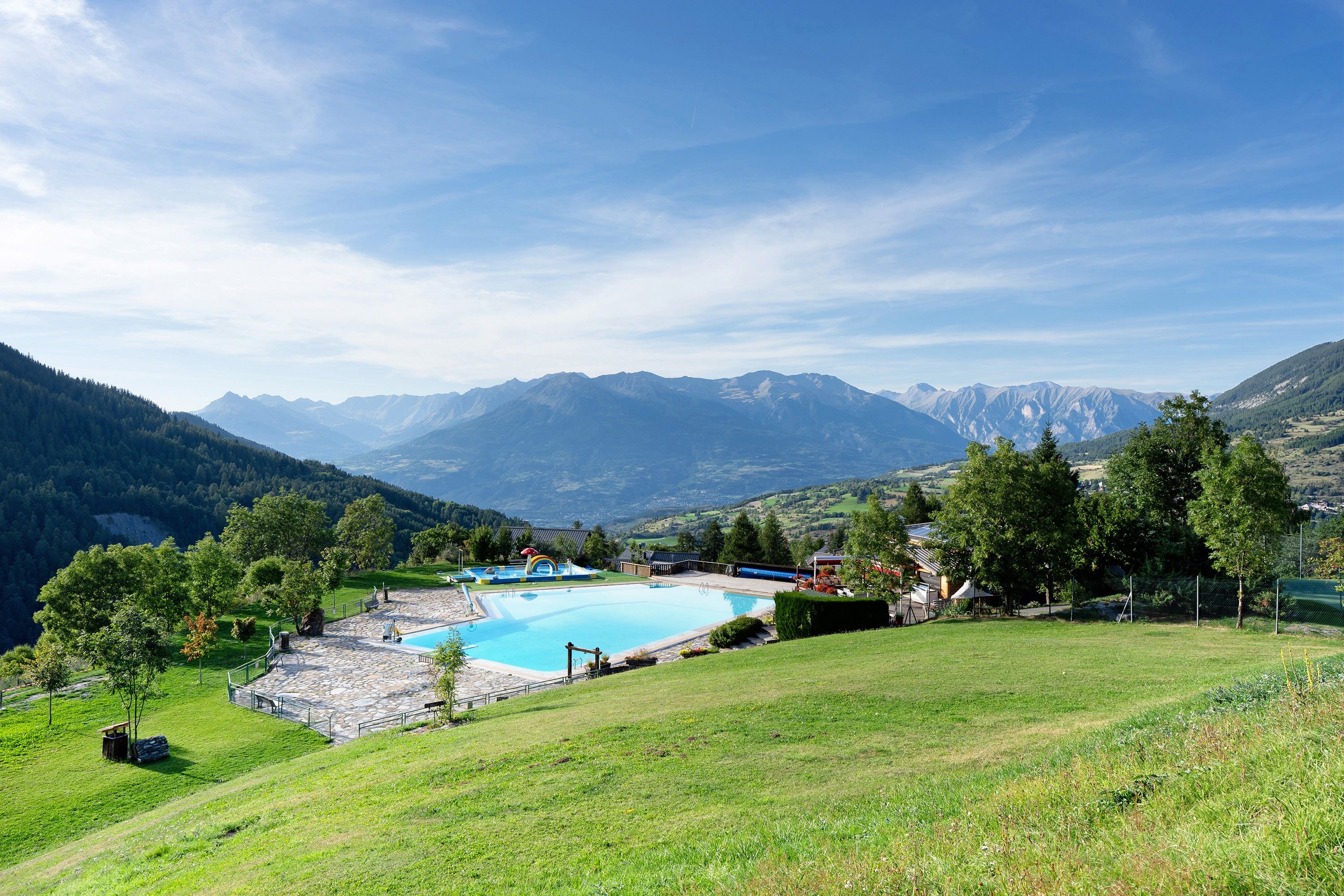 A pool with a mountain backdrop, surrounded by greenery and a clear sky.