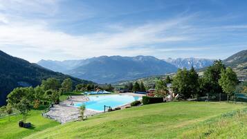 A pool with a mountain backdrop, surrounded by greenery and a clear sky.