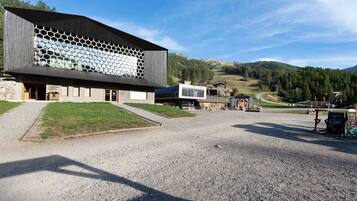 Un bâtiment moderne à la façade hexagonale, avec une allée gravillonnée et un paysage montagneux en arrière-plan.