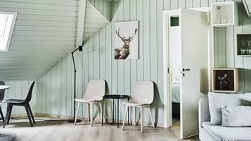 Een kamer met houten vloer, twee stoelen, een kleine tafel, een bank, een schilderij van een hert en een trap.