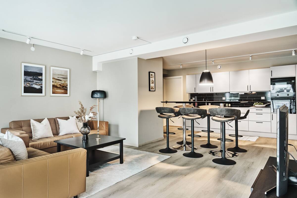 Een moderne woonkamer met een bank, salontafel en barstoelen. Er is een keuken met kasten en een eettafel.