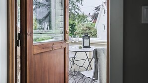 Puerta de madera que da a un balcón con una mesa, sillas, un farol y dos copas de vino.