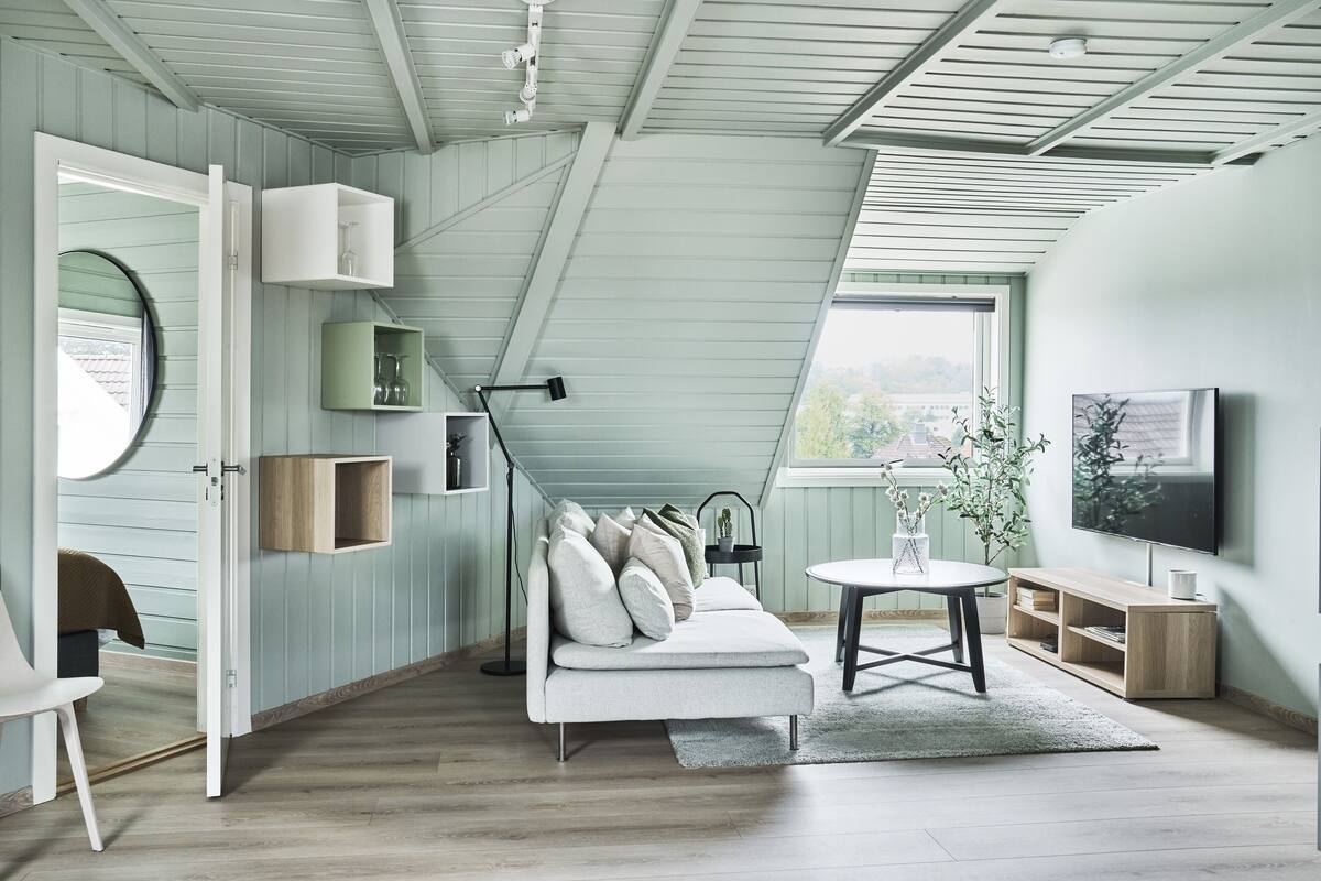 Een moderne woonkamer met een hoge plafond, een witte bank, een ronde tafel, en een tv die aan de muur is bevestigd.