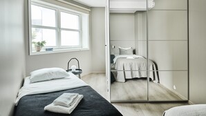 Un dormitorio con cama, mesita de noche, espejo y ventana.