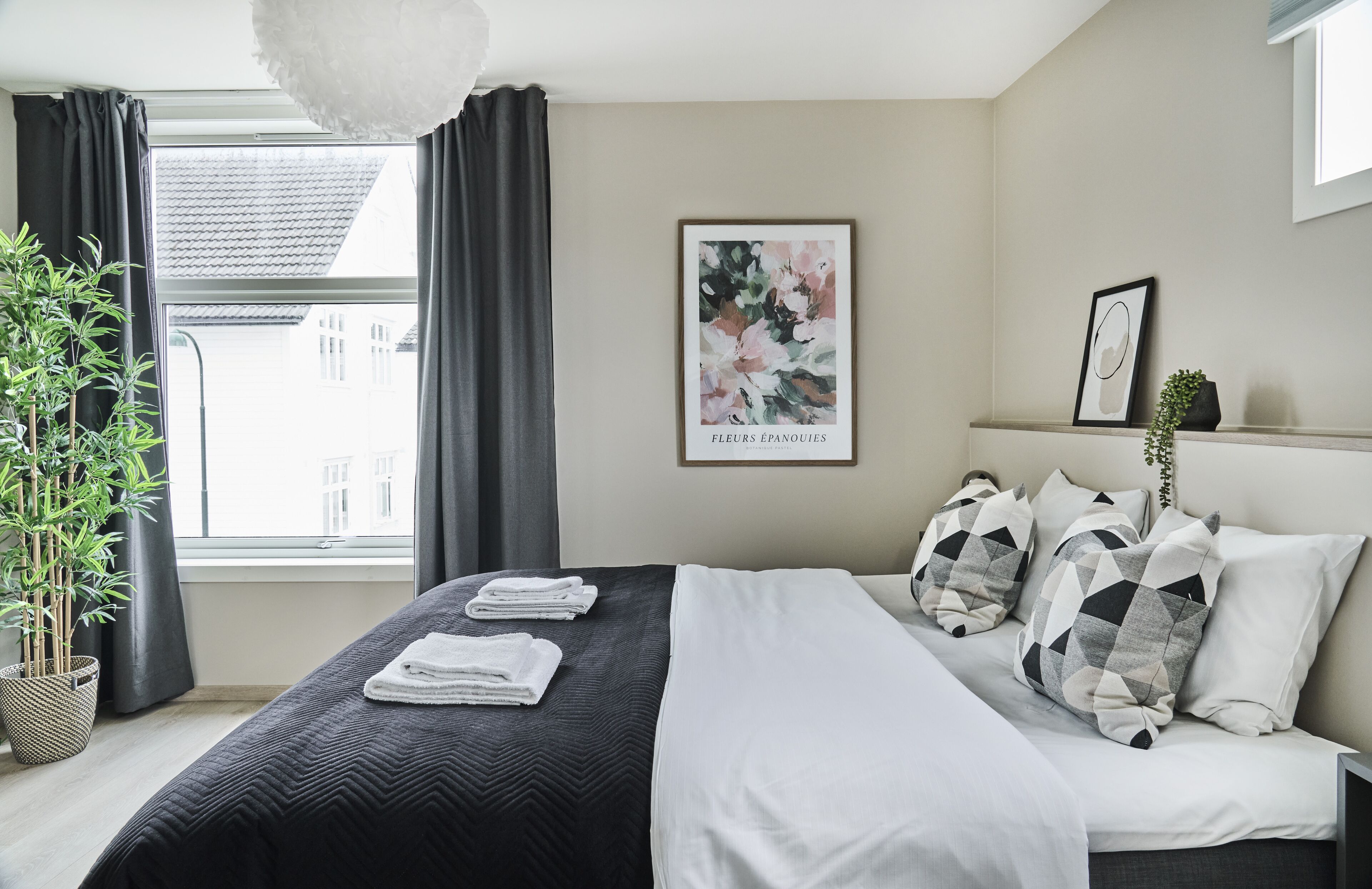 Una cama bien hecha con sábanas blancas, un cojín de diseño blanco y negro, y una obra de arte floral enmarcada en la pared.