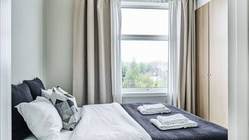 A hotel room with a bed, two pillows, a window with curtains, and a view of greenery outside.