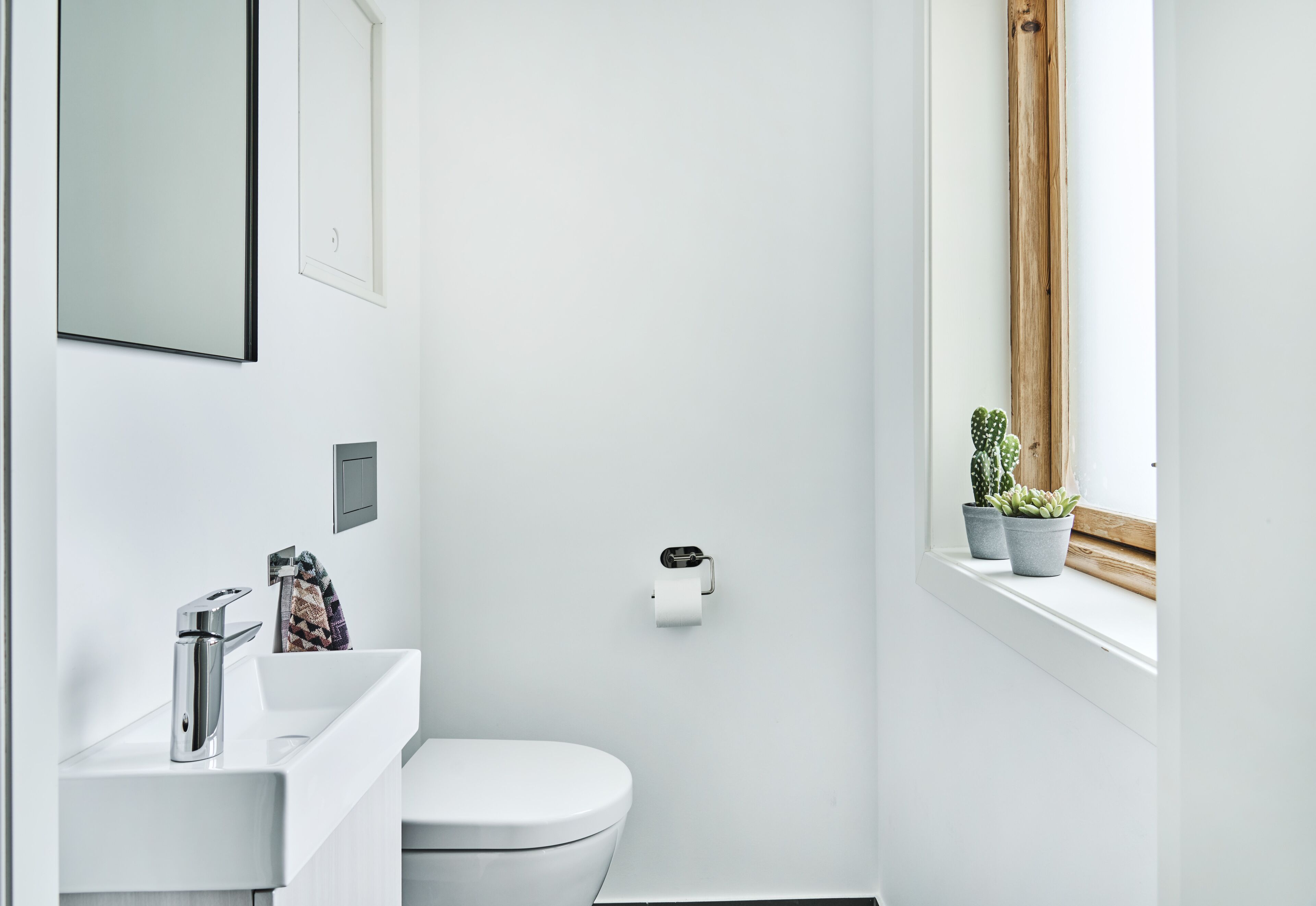 Ein modernes Badezimmer mit einem weißen Waschbecken, einer Toilette und einem Fenster mit Pflanzen.
