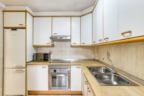 A compact kitchen with white cabinets, a built-in oven, a microwave, and a sink.