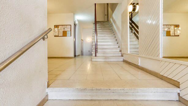 Un escalier avec une rampe, un sol carrelé et des murs ornés de panneaux d’affichage.