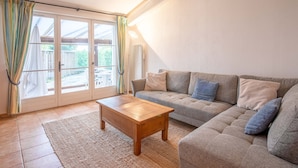 Una sala de estar con un sofá, una mesa de centro de madera y un ventanal corredero que da a un espacio exterior.